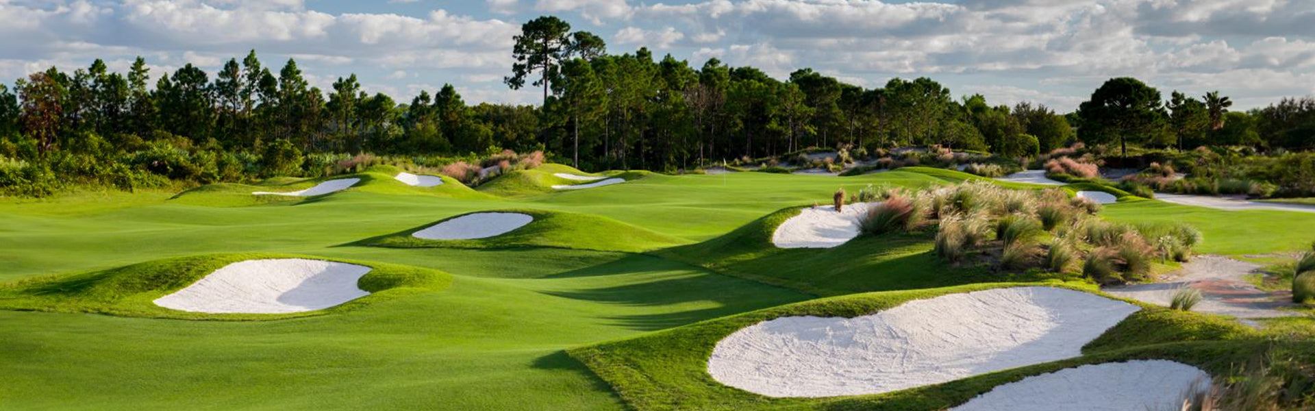 A lush fairway lined with white sand bunkers and native grasses at PGA National in Palm Beach Gardens, Florida, under a partly cloudy sky.