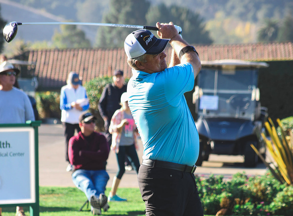 Kenny Perry follows through on a driver swing wearing a Straight Down blue polo at the Straight Down Fall Classic, with spectators and California hills in the background.