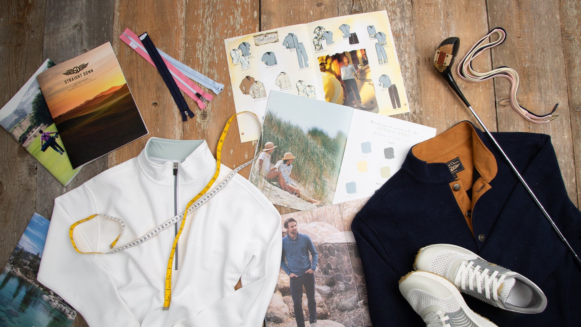 Straight Down apparel samples, design sketches, color swatches, and tools spread across a wooden table during the product development process.