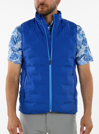Men's Peak Vest in Azurite, on-model front view featuring a royal blue quilted vest with a full zip closure and light blue zip trim detail worn over a blue tropical print polo with gray pants