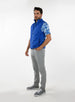 Men's Peak Vest in Azurite, on-model full-length front view featuring a royal blue quilted vest with a full zip closure and light blue zip trim detail worn over a blue tropical print polo with gray pants and gray golf shoes