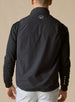 Men's Denver Vest in Black, back model view featuring a black shell with woven logo patch at the upper back, layered over a black long sleeve pullover with light gray pants