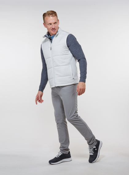 Men's Canyon Vest in Silver, side on-model view featuring a light gray quilted puffer vest with a full zip closure and front zip pocket, styled with a charcoal heather long sleeve, gray pants, and dark shoes