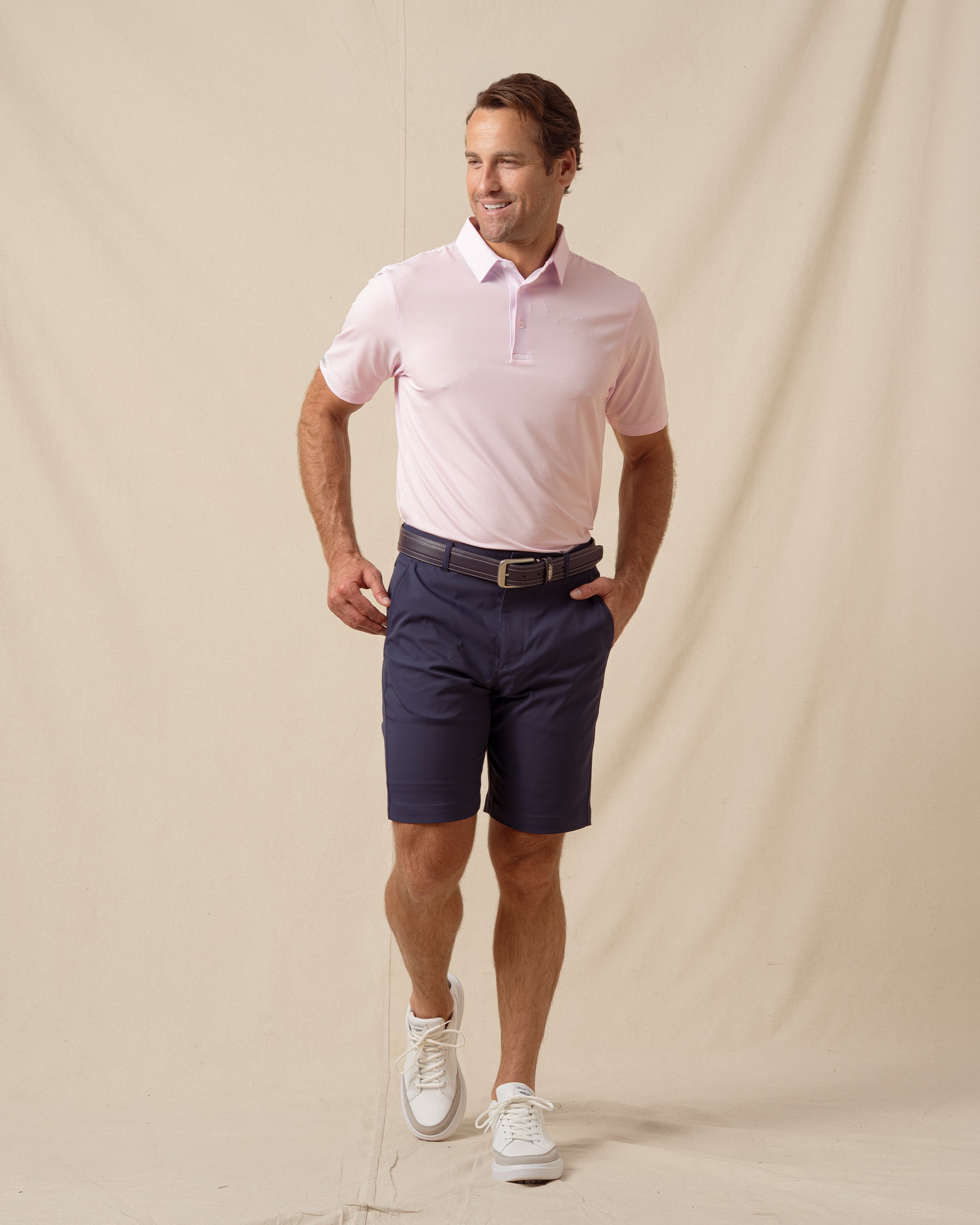 Men’s lilac polo styled with navy shorts, brown belt, and white sneakers