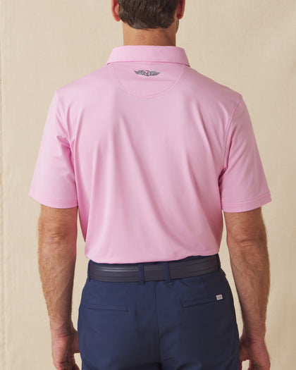 Back view of men’s solid pink polo with collar logo detail, tucked into navy shorts