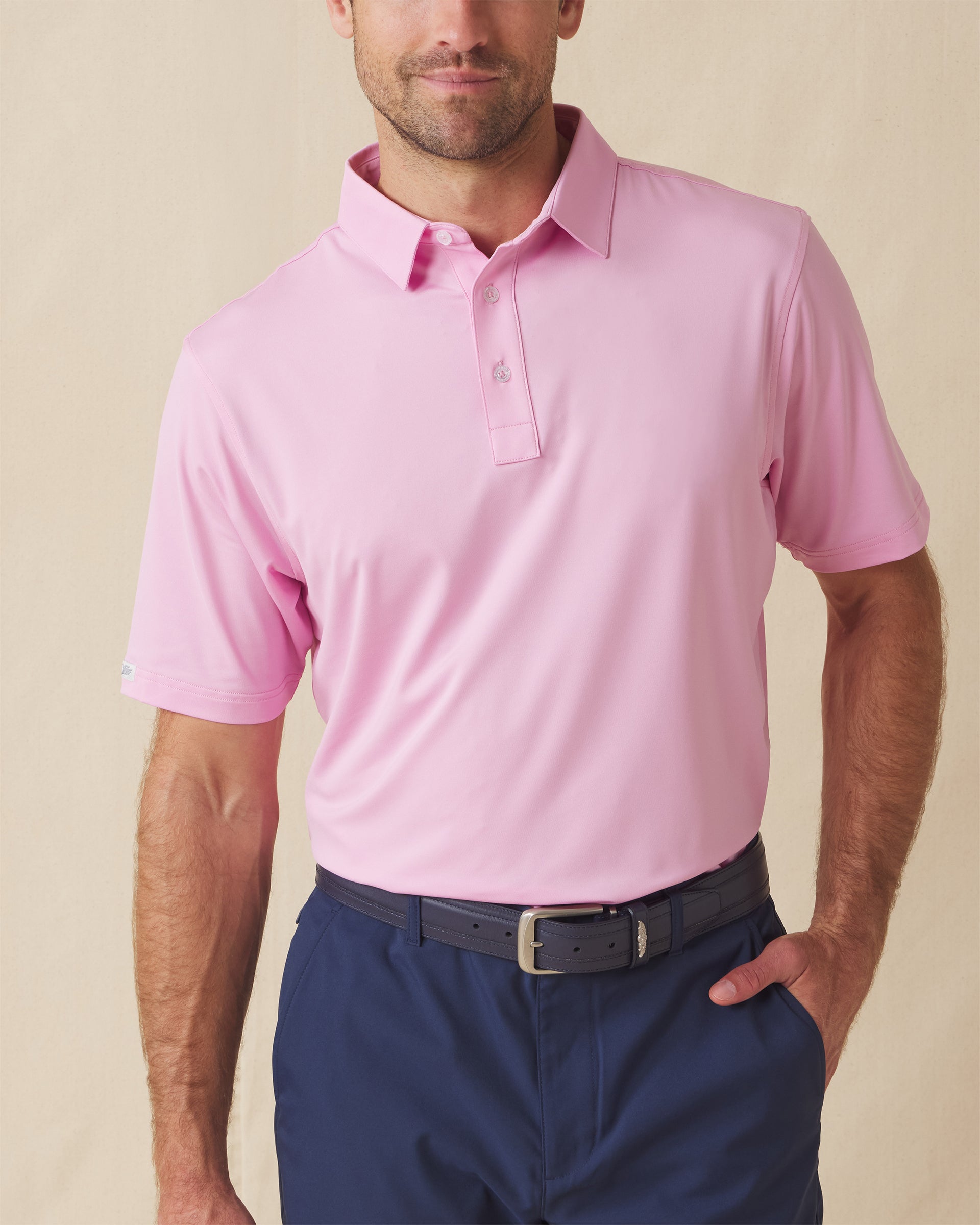 Men’s solid pink polo with short sleeves and button placket, paired with navy shorts