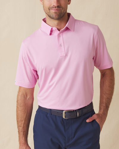 Men’s solid pink polo with short sleeves and button placket, paired with navy shorts