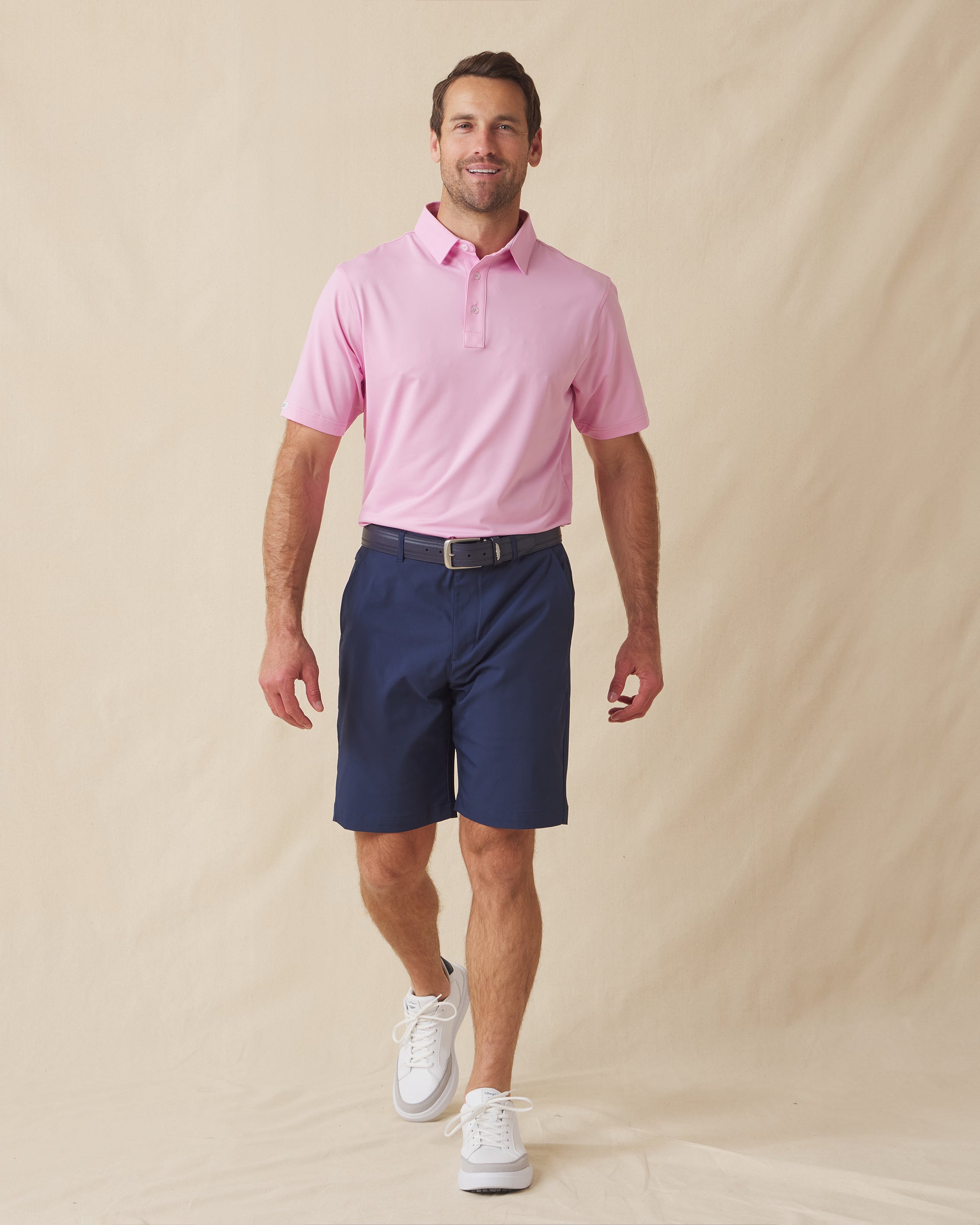 Men’s pink polo styled with navy shorts, brown belt, and white sneakers