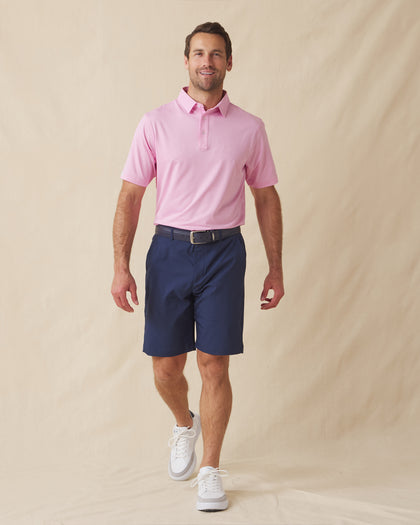 Men’s pink polo styled with navy shorts, brown belt, and white sneakers