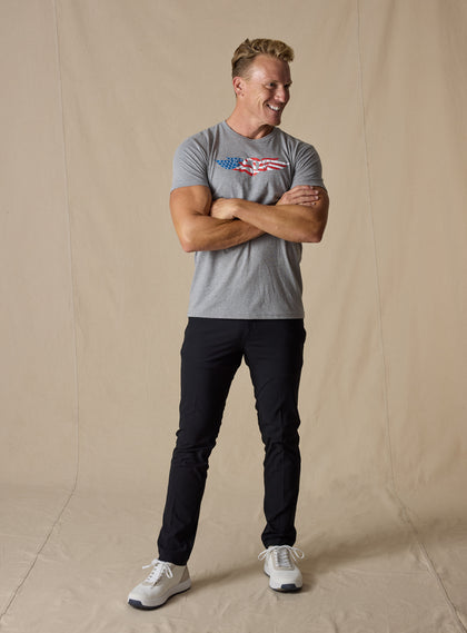 Men's USA Wings Tee in Heather, on model full length front view featuring a heather gray crewneck with an American flag Straight Down logo graphic styled with black pants and white shoes