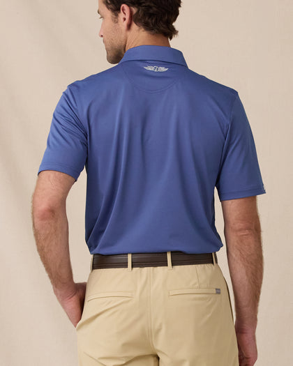 A model shown from the back wearing a blue short-sleeve polo shirt and khaki shorts, photographed against a plain beige studio background.