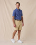 A man modeling a blue short-sleeve polo shirt and beige shorts against a beige fabric backdrop.