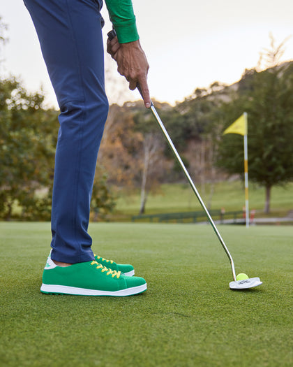 Men's Field V2 Shoe in Green, on-course lifestyle view featuring a golfer putting on the green