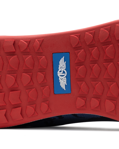 Men's Field V2 Shoe in Camo Indigo, close-up outsole view featuring a red rubber outsole with multi-directional traction lugs and a blue branded logo badge