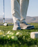 Straight Down Club Golf Shoe in Carbon, on-course lifestyle view showing shoes worn with white pants, golf iron and golf balls in foreground with mountain backdrop