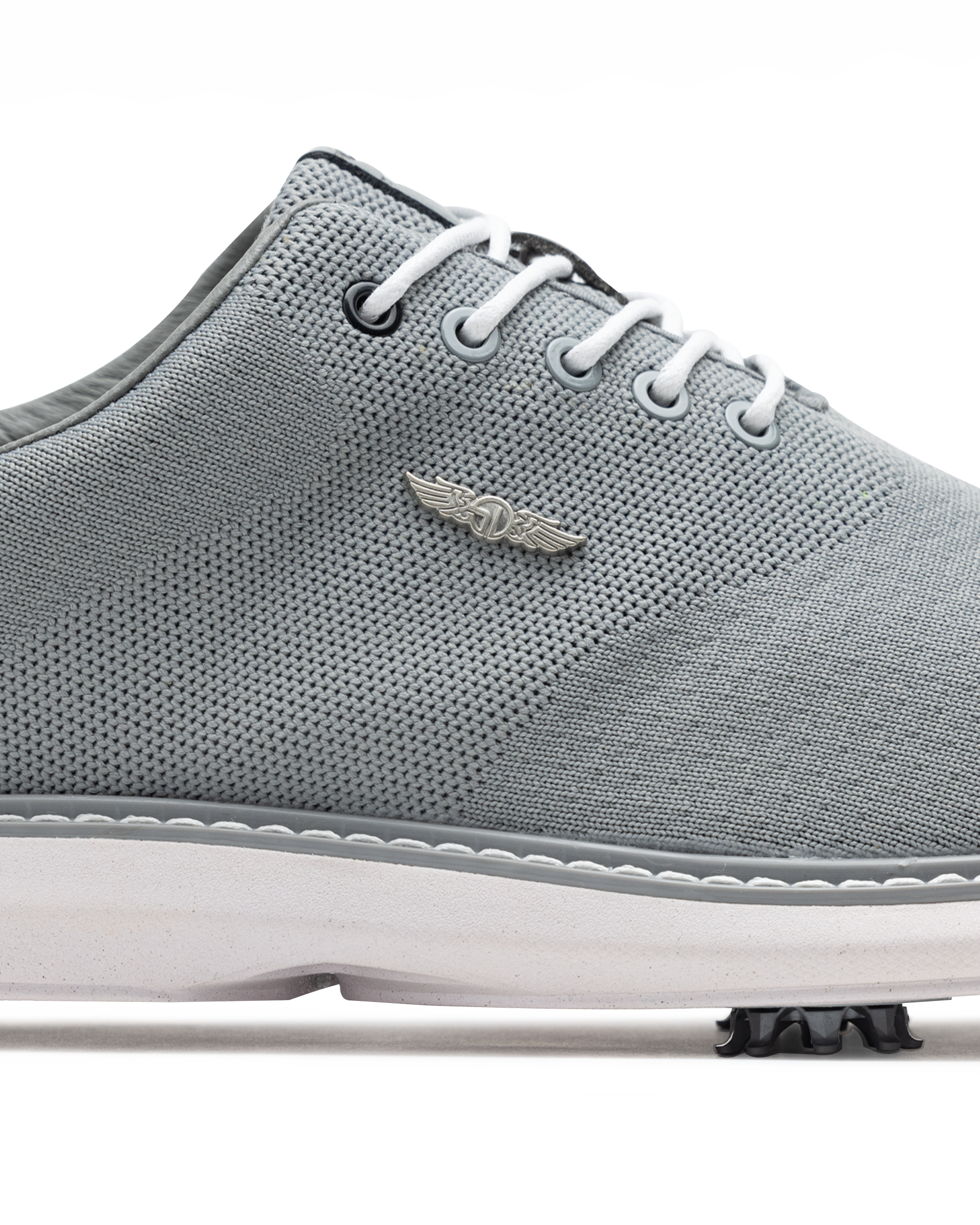 A close-up side view of a light gray knit golf shoe with white laces, a white sole, and a small silver wing logo on the side.