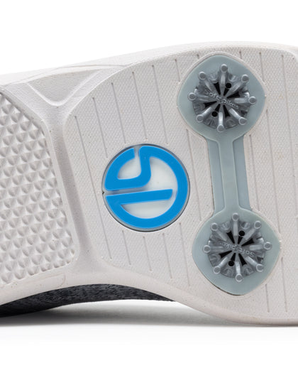 Men's Challenger Shoe in Carbon, close-up outsole view featuring a white rubber outsole with gray spike cleats and a blue branded logo badge detail