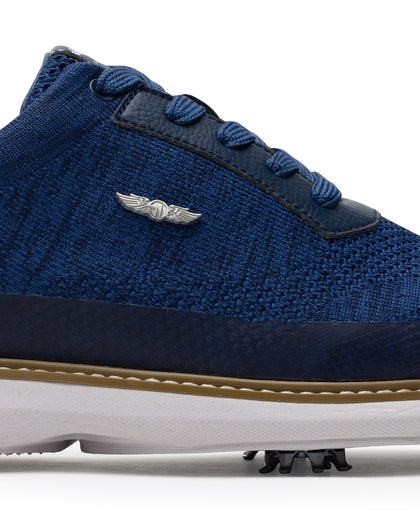 Men's Challenger Shoe in Indigo, close-up side view featuring a navy knit upper highlighting the silver wing logo badge, navy leather lace stay, and tan welt stitch detail with white midsole and spiked outsole