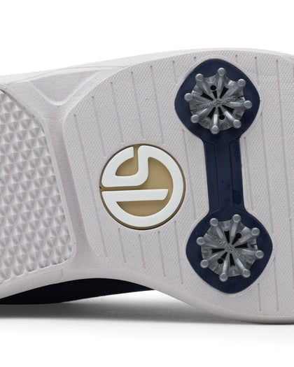 Men's Challenger Shoe in Indigo, close-up outsole view featuring a white rubber outsole with navy spike cleats and a gold and white branded logo badge detail