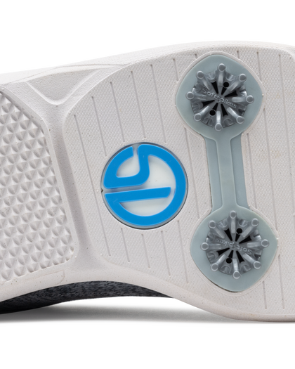 Men's Challenger Shoe in Carbon, close-up outsole view featuring a white rubber outsole with gray spike cleats and a blue branded logo badge detail