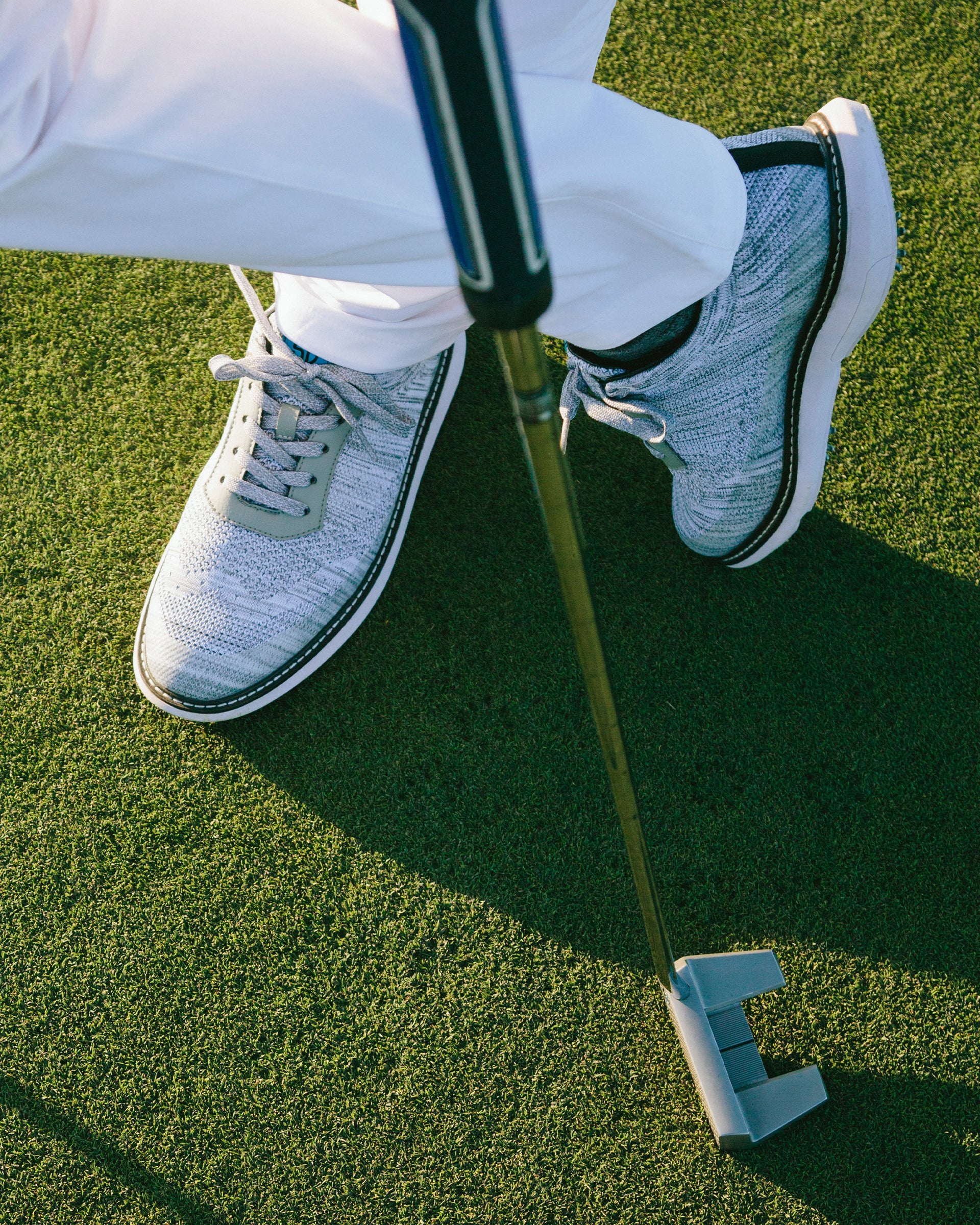 Men's Challenger Shoe in Carbon, on-course lifestyle view featuring a golfer putting on the green wearing heathered gray knit shoes with gray laces, white midsole, and black welt stitch detail with white pants
