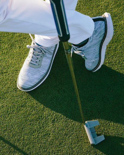 Men's Challenger Shoe in Carbon, on-course lifestyle view featuring a golfer putting on the green wearing heathered gray knit shoes with gray laces, white midsole, and black welt stitch detail with white pants