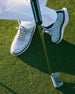 Men's Challenger Shoe in Carbon, on-course lifestyle view featuring a golfer putting on the green wearing heathered gray knit shoes with gray laces, white midsole, and black welt stitch detail with white pants