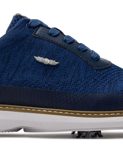 Men's Challenger Shoe in Indigo, close-up side view featuring a navy knit upper highlighting the silver wing logo badge, navy leather lace stay, and tan welt stitch detail with white midsole and spiked outsole