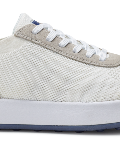 Men's Rally Shoe in White, detail close-up view featuring the white knit upper texture, light gray suede overlay at the toe box, white lace-up closure, and white midsole with navy outsole visible at the base