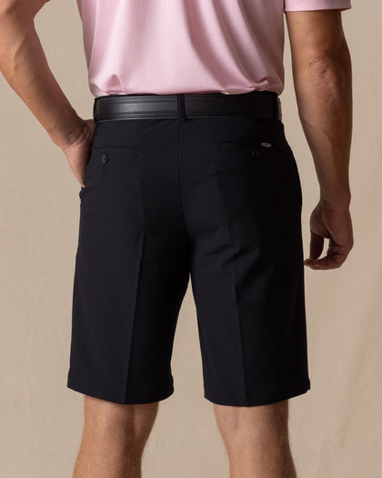 Men's Drake Short in Black, back model view featuring button-welt back pockets with tonal winged logo detail, styled with a black belt and pink polo