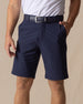 Men's Drake Short in Indigo, front model view featuring a flat-front silhouette in a rich navy blue colorway, styled with a navy belt and white polo