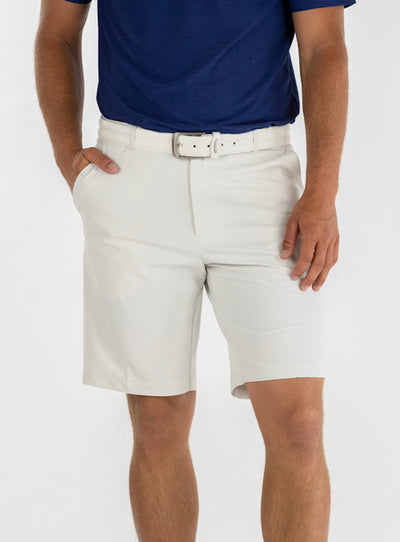 Men's Drake Short in Stone, front model view featuring a flat-front silhouette in a warm off-white colorway, styled with a white belt and navy polo