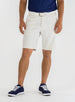 Men's Drake Short in Stone, front model view featuring a flat-front silhouette in a warm off-white colorway, styled with a white belt, navy polo, and navy golf shoes