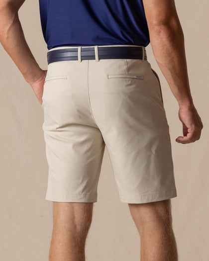 Men's Maverick Twill Short in Cashew, back model view featuring a light tan solid twill fabric with welt back pockets, styled with a navy polo and navy belt