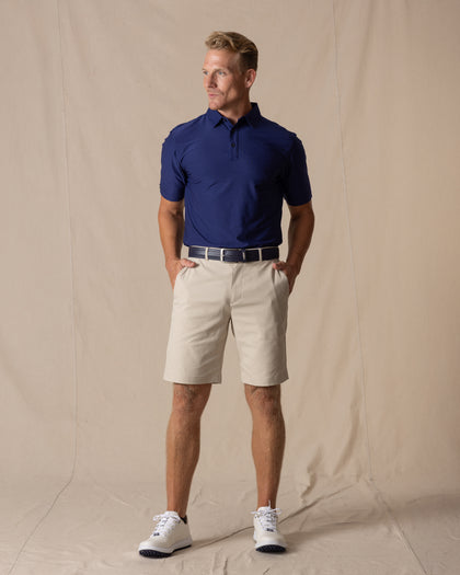 Men's Maverick Twill Short in Cashew, full length model view featuring a light tan solid twill fabric, styled with a navy polo, navy belt, and white shoes