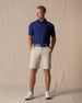 Men's Maverick Twill Short in Cashew, full length model view featuring a light tan solid twill fabric, styled with a navy polo, navy belt, and white shoes