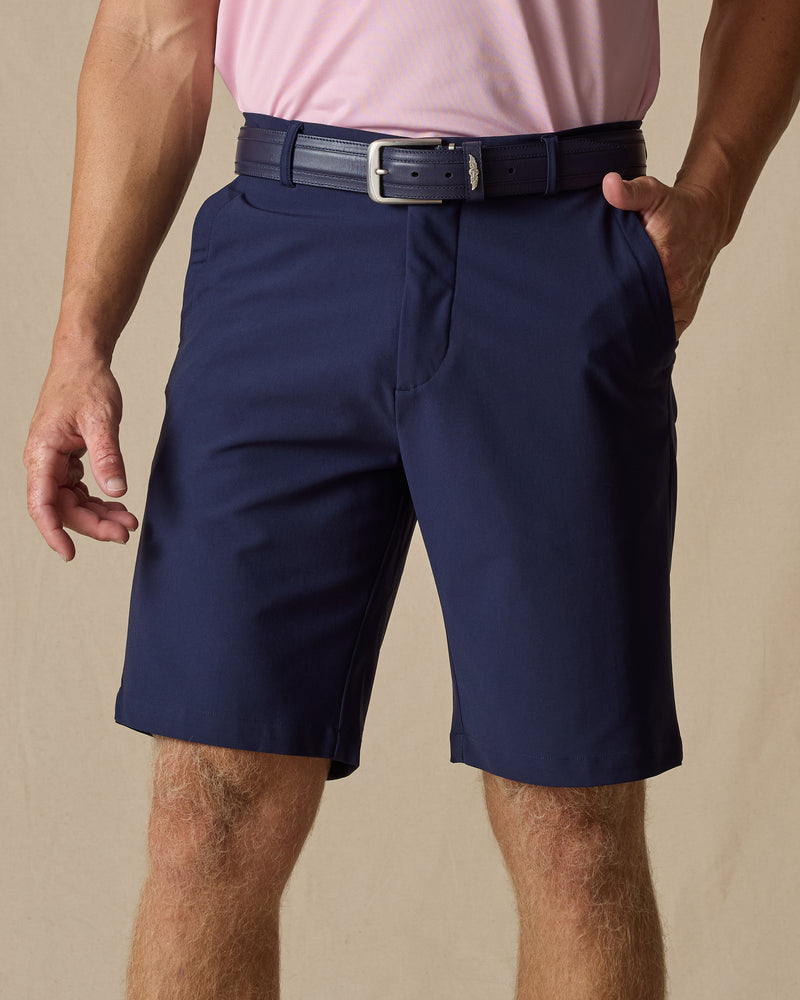 Men's Maverick Twill Short in New Indigo, front model view featuring a navy solid twill fabric with side slash pockets, styled with a pink polo and navy belt
