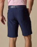 Men's Maverick Twill Short in New Indigo, back model view featuring a navy solid twill fabric with buttoned welt back pockets and tonal logo detail, styled with a pink polo and navy belt