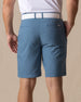 Men's Maverick Twill Short in Petrol, back model view featuring a medium blue solid twill fabric with welt back pockets, styled with a white polo and white belt