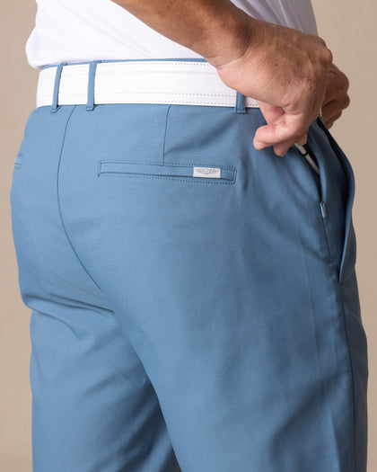 Men's Maverick Twill Short in Petrol, detail close-up back view featuring a medium blue solid twill fabric, tonal logo badge, and zippered interior pocket, styled with a white belt