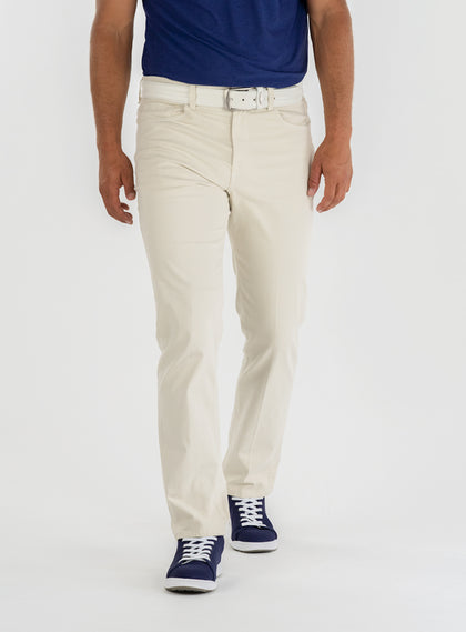 Men's Clemson Pant in Stone, on-model front view featuring a light tan five-pocket style with a button closure and white belt worn with a navy polo and navy golf shoes