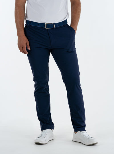 Men's Quest Pant in Indigo, front on-model view featuring navy pants with a button waistband closure and side pockets, styled with a white shirt and white shoes