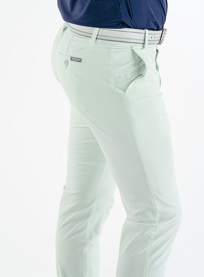 Men's Quest Pant in Light Mint, close-up side and back detail view featuring the button-closure back pocket with a small logo tab, styled with a white belt and navy shirt