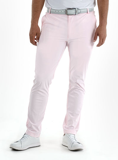 Men's Quest Pant in Light Pink, front on-model view featuring light pink pants with a button waistband closure and side pockets, styled with a white polo, gray belt, and white shoes