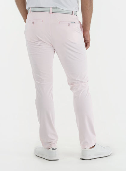 Men's Quest Pant in Light Pink, back on-model view featuring light pink pants with button-closure back pockets and a small logo tab, styled with a white polo, gray belt, and white shoes
