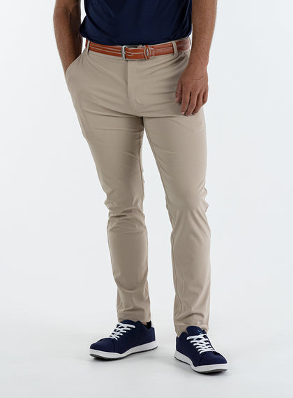 Men's Quest Pant in Light Khaki, front on-model view featuring khaki pants with a button waistband closure and side pockets, styled with a navy shirt, brown belt, and navy shoes