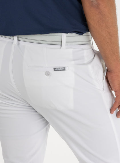 Men's Quest Pant in White, close-up back detail view featuring the button-closure back pocket with a small embroidered logo tab, styled with a gray belt and navy shirt