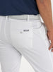 Men's Quest Pant in White, close-up back detail view featuring the button-closure back pocket with a small embroidered logo tab, styled with a gray belt and navy shirt