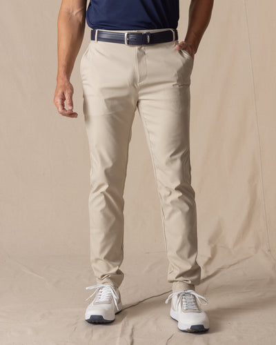  Men's Maverick Twill Pant in Cashew, front view on model featuring a solid cashew color with navy belt and white golf shoes