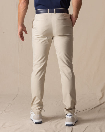 Men's Maverick Twill Pant in Cashew, back view on model featuring a solid cashew color with navy belt and white golf shoes